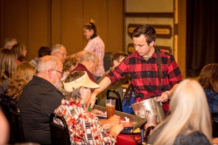 A young man serving dinner while audiences enjoys A Shepherd’s Christmas Carol Dinner Show at  the Playhouse Theatre, Shepherd of the Hills, Branson, MO.