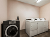 A hotel guest laundry room with a black washer next to a set of white washers and dryers at the Country Inn & Suites.