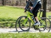 Two people riding lime green bicycles on a paved path through a park on a sunny day.